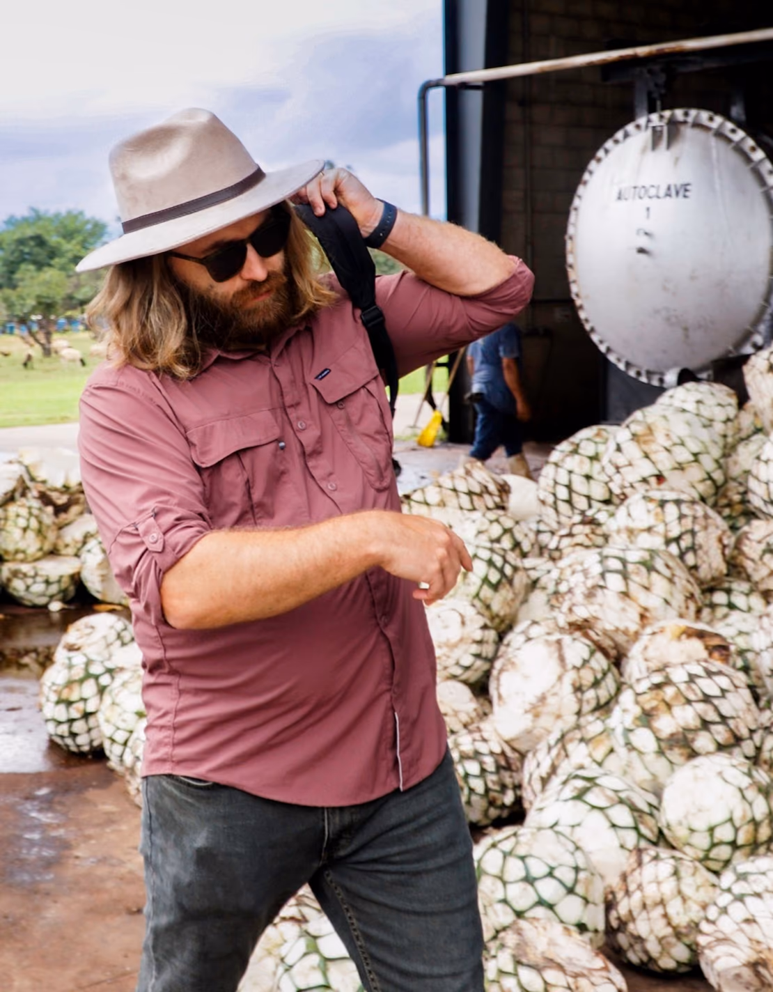 A man in a hat standing among piles of harvested agave piñas