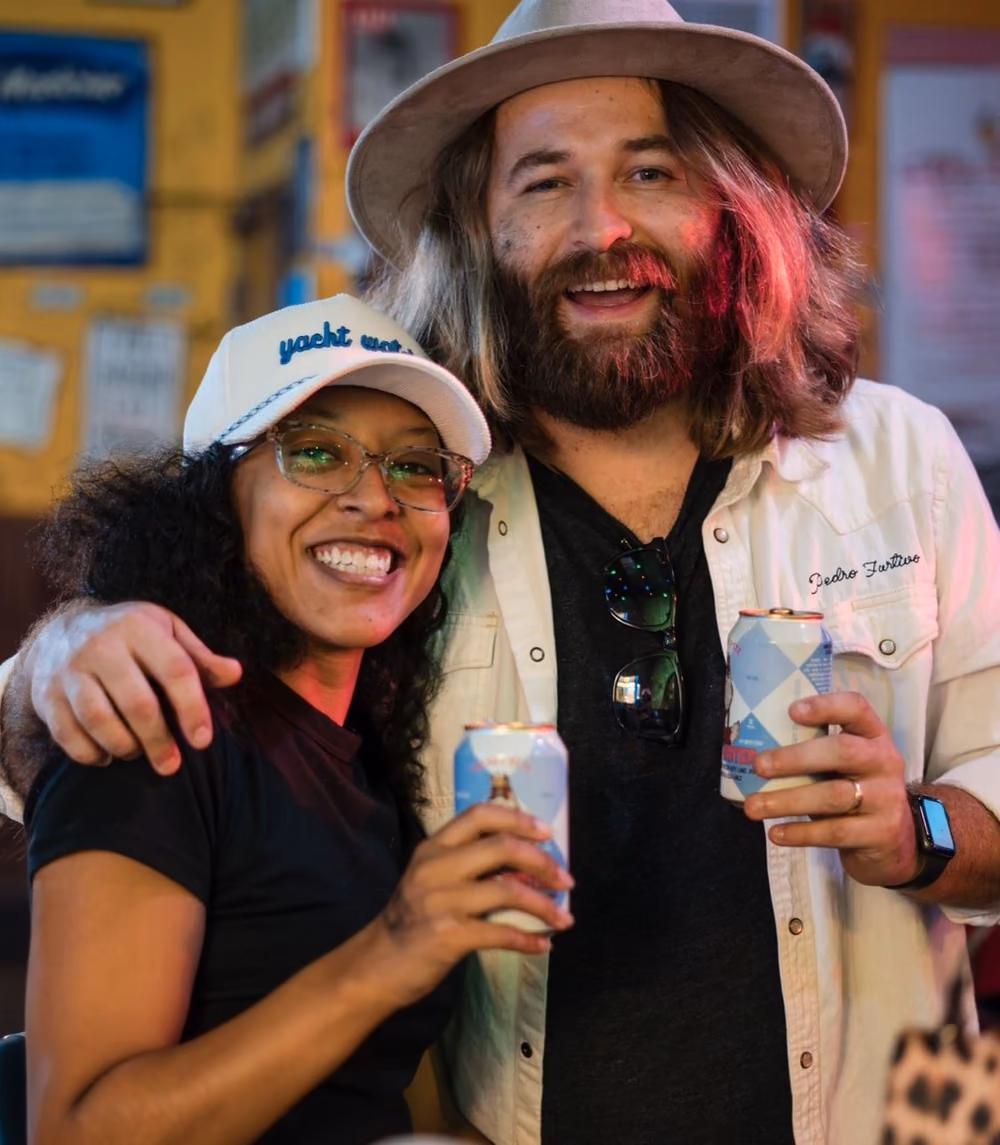 Two guests smiling with Yacht Water cans at the Tin Roof night