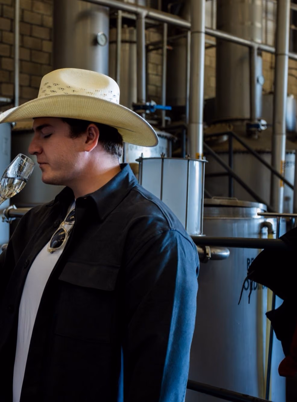 Two men in cowboy hats nosing a glass in front of the stills