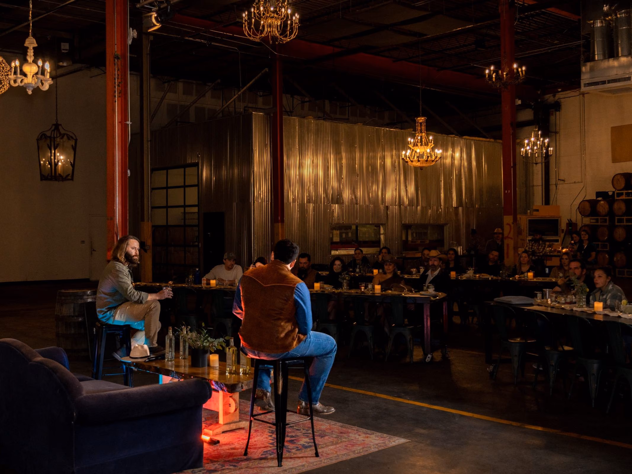 A warm barrel room with long tables and chandeliers