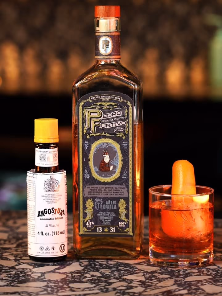 A bottle of Pedro Furtivo 1331 Añejo beside bitters and an Old Fashioned with an orange peel