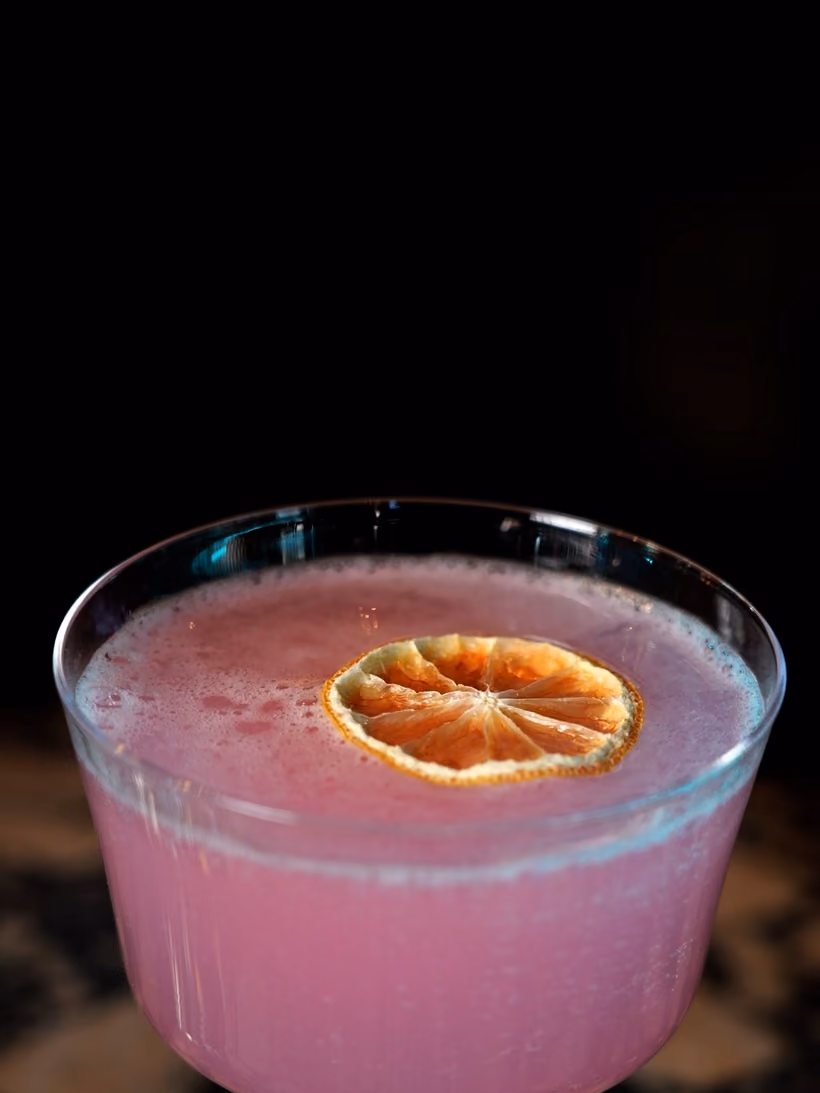 A pink cocktail in a coupe with a dried orange slice