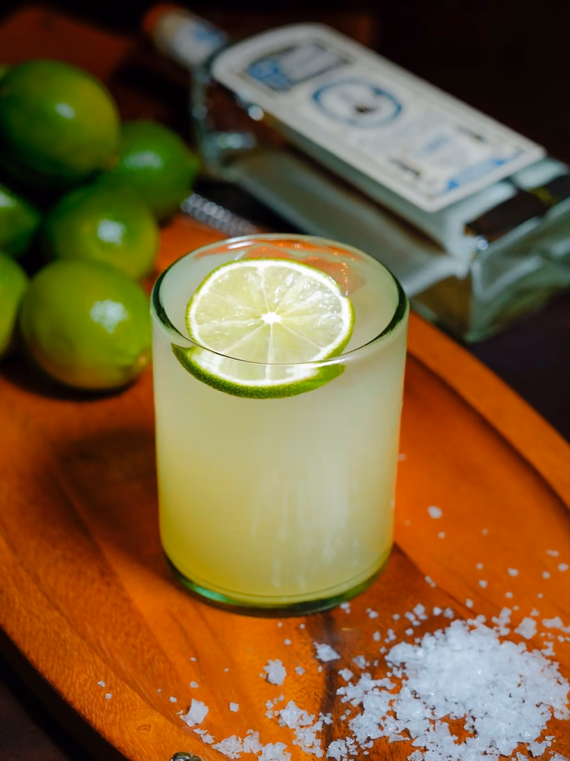 A Margarita Furtivo on a wooden tray with limes and coarse salt