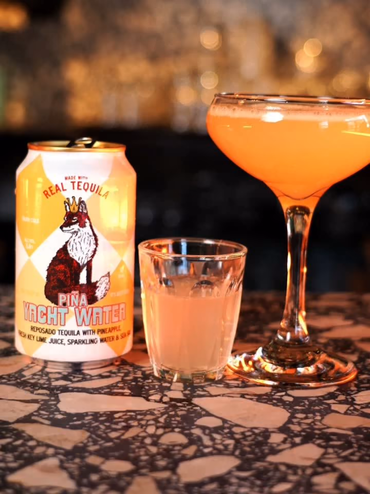 A Piña Pornstar Martini beside a Yacht Water Piña can on a terrazzo bar
