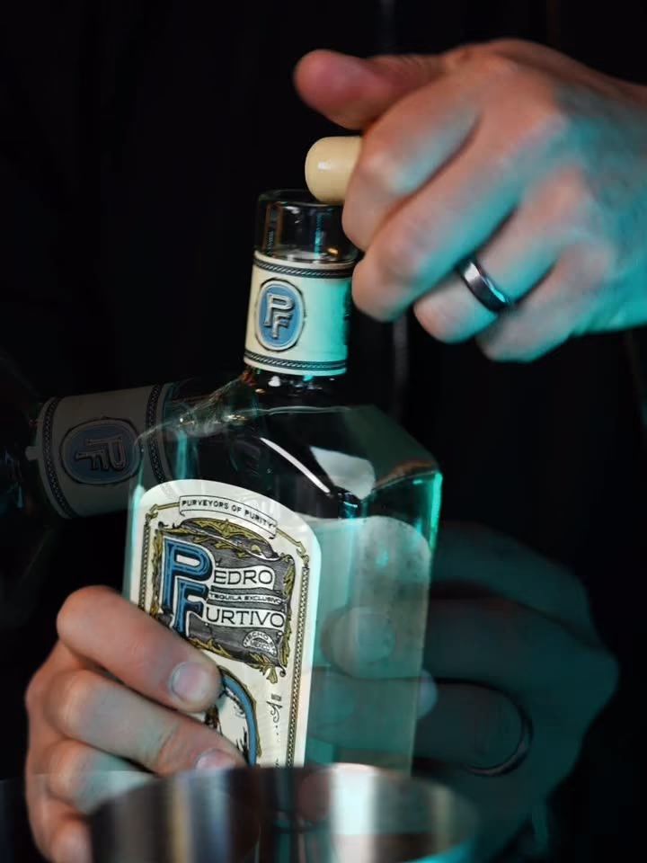 A bartender holding a bottle of Pedro Furtivo Blanco over a cocktail shaker